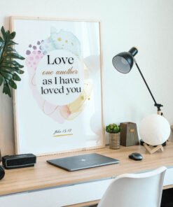 Love One Another Wall Art in a black frame on the wooden desk next to a black lamp and a laptop