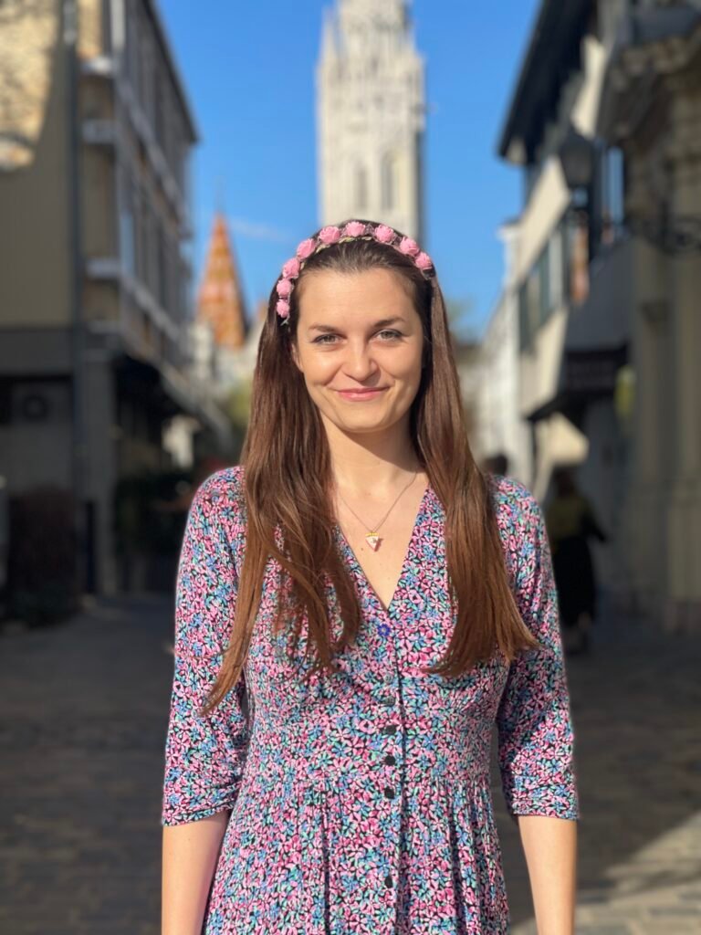 woman wearing floral dress and pink flowers on her head, white buildings behind her